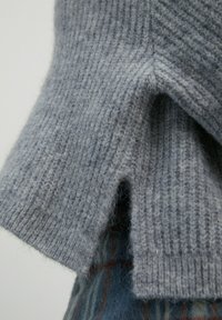 Grau gestrickter Pullover im Close-up, mit einem gerippten Muster und einem V-Ausschnitt am Saum; weiche, wuschelige Faser mit subtiler Farbvariation.