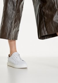 Vita lädersneakers med snörning, med rund tå och en strukturerad sula. Bärs tillsammans med mörka, blanka byxor med vida ben.