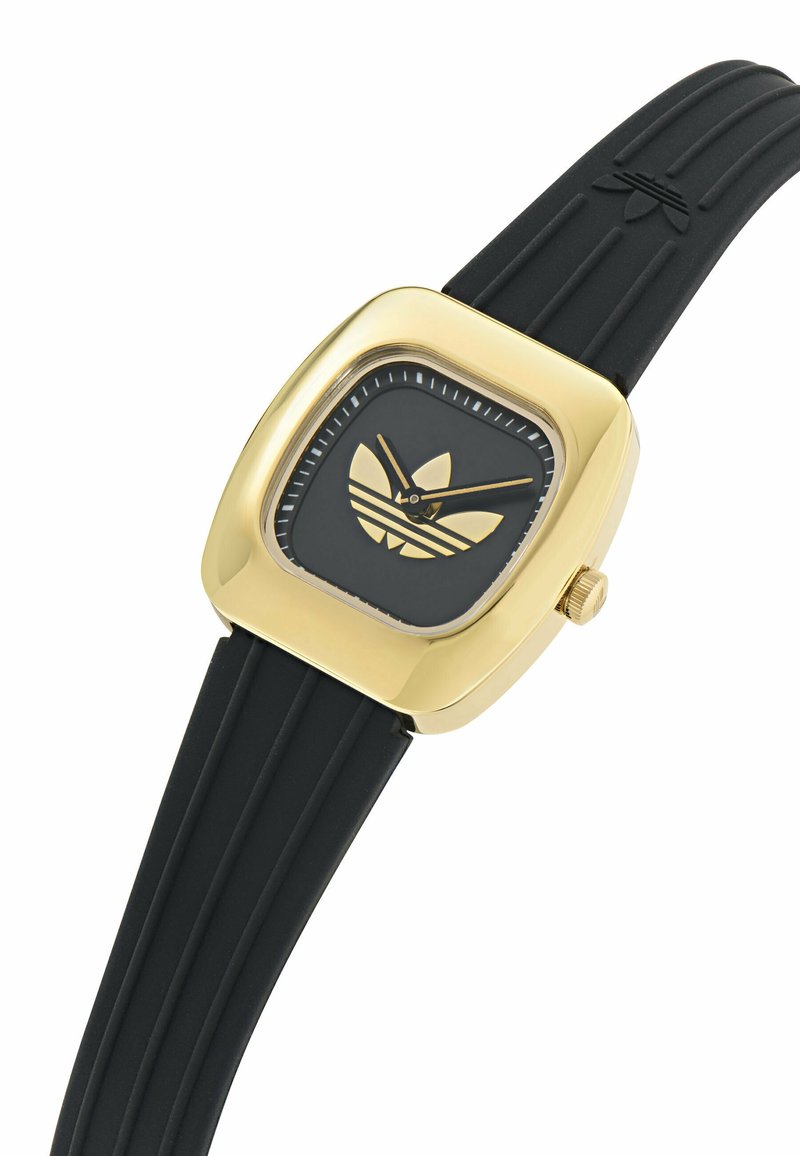 Vierkante horloge met gouden tint, een zwarte wijzerplaat, een kenmerkend logo en een zwarte rubberen band met geribbeld detail. Klassiek ontwerp met minimalistische accenten.