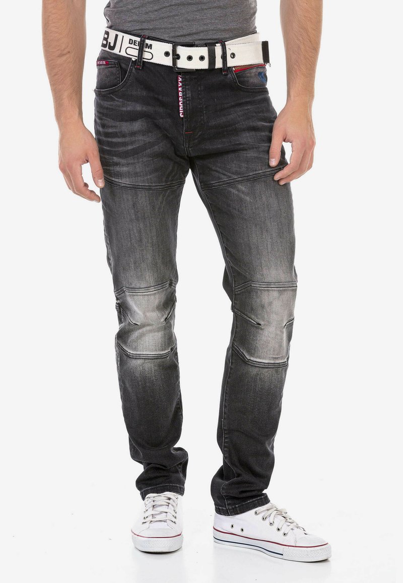 Schwarze Jeans aus Denim mit verwaschenen Stellen und Nähdetails, getragen mit einem weißen Gürtel und weißen Sneakers. Slim-Fit-Design.