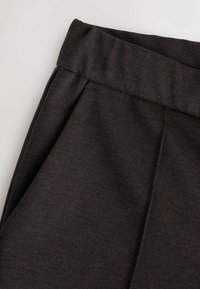 Pantaloni in tessuto elastico grigio scuro con cintura larga, caratterizzati da cuciture verticali e tasche, che mostrano una texture liscia e opaca.