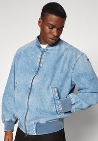 Ανοιχτό μπλε τζιν μπόμπερ τζάκετ με μπροστινό φερμουάρ, ραμμένες μανσέτες και πλαϊνές τσέπες. Διαθέτει αντίθετη ραφή και ραμμένο γιακά.