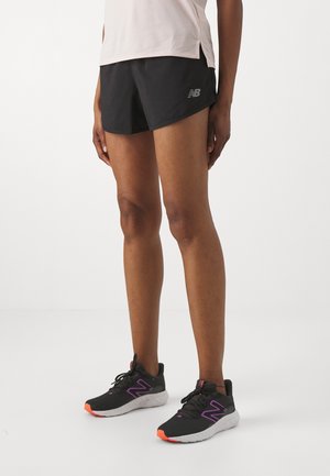 Sorte sportsshorts med et New Balance-logo, parret med sorte løbesko med lilla detaljer og orange såler.