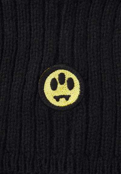 Cappello in maglia nera con una patch gialla rotonda che presenta un impronta di zampa nera e un design di osso. Tessuto testurizzato con righe verticali.