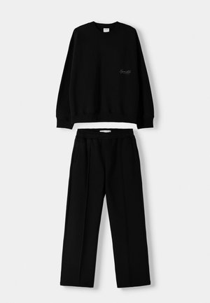 Black sweatshirt with ribbed cuffs and relaxed fit, paired with black trousers featuring an elastic waistband and side pockets. Smooth texture.