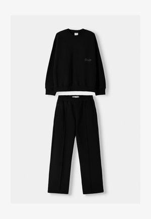 Black sweatshirt with ribbed cuffs and relaxed fit, paired with black trousers featuring an elastic waistband and side pockets. Smooth texture.
