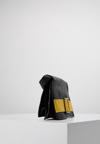 Borsa a mano in pelle nera con finitura texturizzata, caratterizzata da un'importante accentuazione in pelle gialla e hardware in tonalità argento, forma squadrata.