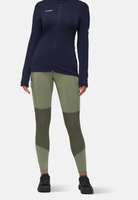 Marine blauw zip-up jack en olijfgroene leggings. Het jack heeft lange mouwen en een getailleerd ontwerp. De leggings hebben contrasterende panelen en een gladde textuur.