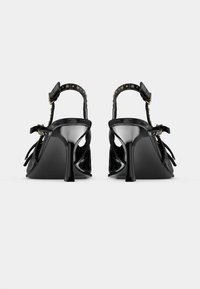 Sandali neri con tacco alto e retro aperto, caratterizzati da fasce sottili e dettagli con borchie. I tacchi sono eleganti e lucidi, con un design a punta.