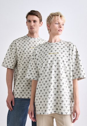 Oversized short-sleeve t-shirts, beige with black logo patterns. Features a round neck and visible stitching. Text reads "CARLO GULLO."