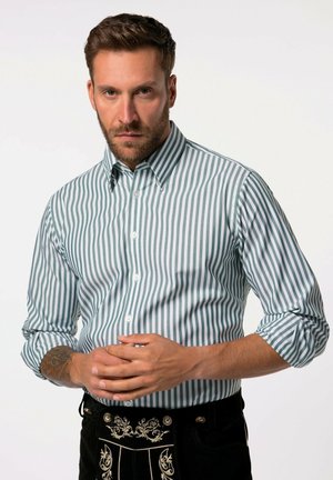 Striped shirt in green and white cotton with a button-down collar. Features rolled-up sleeves and a tailored fit. Paired with dark trousers.