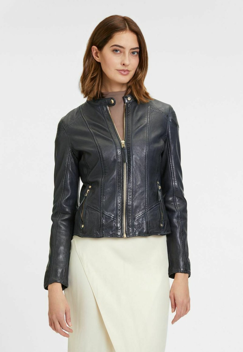 Giacca in pelle nera con design aderente, zip frontale, due tasche laterali e dettaglio a scatto sul colletto. Texture liscia e linee pulite.