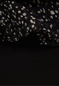 Tissu noir avec un bord froncé avec des pois blancs irréguliers, créant un contraste texturé entre matériau lisse et froncé.