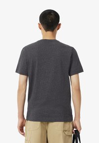 T-shirt corto grigio scuro con colletto rotondo e una leggera texture, abbinato a pantaloni cargo beige. La vista posteriore mostra i dettagli delle cuciture delle spalle.