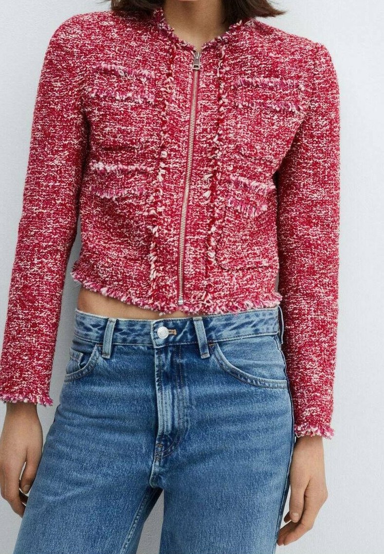Femme portant une veste courte rouge texturée avec une fermeture éclair à l'avant et des poches plaquées, associée à un jean bleu taille haute.