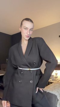 Blazer preto de abotoamento duplo com lapelas largas e botões grandes, ajustado à cintura com um cinto branco. Tecido macio com um corte descontraído.