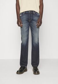 Mörkblå denimjeans med rak benpassform, som har en urtvättad design, fem fickor och knäppning. Bärs med svarta skor.