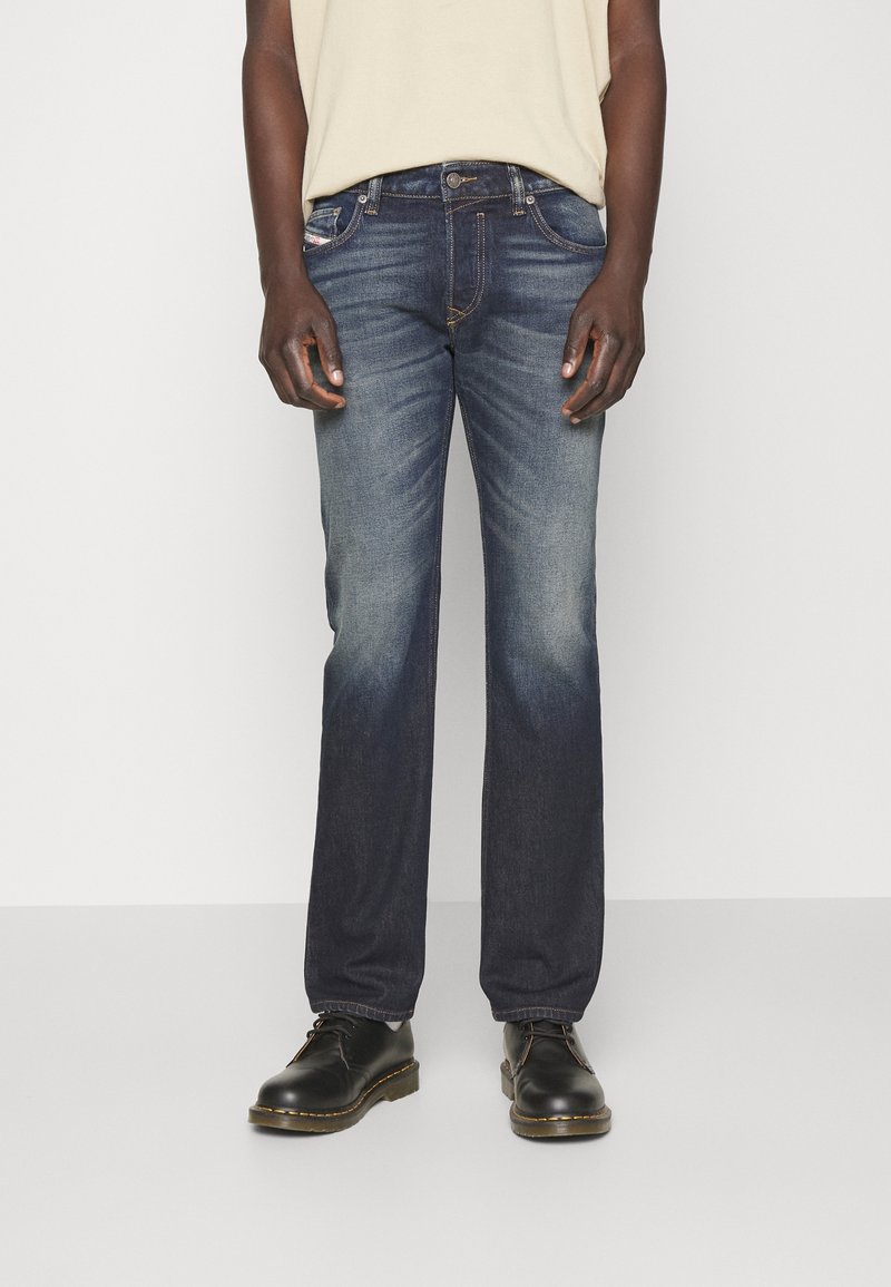 Mörkblå denimjeans med rak benpassform, som har en urtvättad design, fem fickor och knäppning. Bärs med svarta skor.