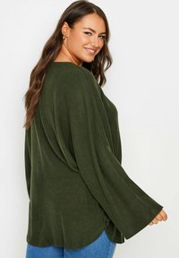 Olivgrön, oversized tröja med långa ärmar och rund halsringning. Mjuk, strukturerad tyg och sprund på fållen, kombinerad med blå jeans.