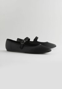 Ballerines noires à bout pointu, texture lisse et une seule bride ajustable avec une boucle ronde. Design élégant avec des accents minimaux.