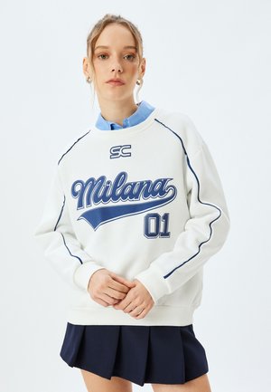 Hvid sweatshirt med blå accenter, prydet med grafikkerne "Milana" og "01". Ribbet manchetter, rund hals, lagt over en lyseblå skjorte med krave.