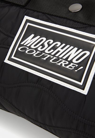 Melnis kvadrāts auduma soma ar izteiktu baltu logo uzlīmi ar tekstu "MOSCHINO COUTURE!" un melnu kniedēšanas aparatūru.