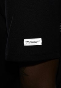 Camiseta atlética negra hecha de material sintético con mangas cortas. Presenta una etiqueta blanca que dice "NIKE PERFORMANCE SPORT APPAREL."