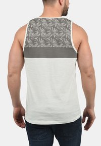 Herren Tanktop mit einem grauen, floral gemusterten Rückenteil, einem einfarbigen, hellgrauen unteren Bereich und kontrastierenden Abnähern entlang der Arme und des Halses.