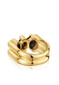 Anillo en tono dorado con un diseño curvado y elegante, adornado con dos acentos de piedras negras redondas incrustadas en una superficie pulida.