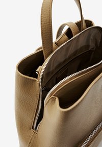 Tan lederen tas met een gestructureerde vorm, dubbele handvatten aan de bovenkant en een ritscompartiment. Binnenin heeft de tas een gevoerde voering met een klein zakje.