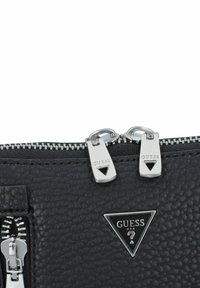 Bolso de cuero negro texturizado con herrajes plateados, que presenta dobles cremalleras y una placa de logo triangular. El patrón tiene un acabado de grano de piedra.
