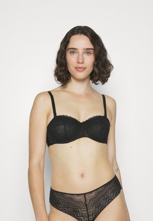 Sujetador negro de encaje con aro, bordes decorativos con ondas y tirantes ajustables. Braguitas a juego de encaje geométrico negro con textura transparente.