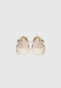 Beige semskede sneakers med hvite teksturerte gummisåler, med dekorative sløyfebeslag og en avrundet bakdesign.