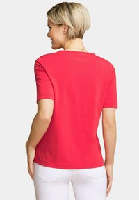 Rode T-shirt met korte mouwen van zachte stof, met een ronde hals en een ontspannen pasvorm, gecombineerd met witte broek en minimalistische sieraden.