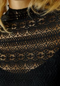 Schwarzes Spitzenoberteil mit intricaten Blumen- und geometrischen Mustern, hochgeschlossenem Design und halbtransparenter Textur.
