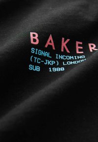 Černé tričko s nápisem "BAKER" v růžové barvě a dalším textem v modré, vyrobené z hladkého bavlněného materiálu a s volným střihem.