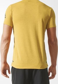 Camiseta deportiva amarilla con un patrón texturizado, mangas cortas y un escote redondeado. Incluye una marca minimalista en el hombro.
