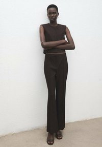 Donkerbruine mouwloze top en bijpassende hoge taille broek. Gladde stof met een getailleerde pasvorm. Eenvoudig ontwerp, rechte pijp stijl.