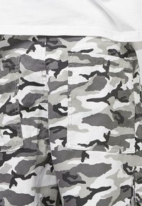 Maskovací cargo šortky v odstínech šedé a bílé, s velkými bočními kapsami a lehkým texturovaným materiálem.