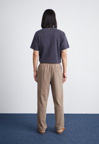 Graues Baumwoll-T-Shirt mit kurzen Ärmeln und rundem Ausschnitt, kombiniert mit beigen, elastischen Stoffhosen mit weichem Material und einer Gesäßtasche.