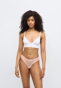 Haut blanc style bralette avec fines bretelles ; string en dentelle rose avec motif de cœurs et bords festonnés. Texture lisse partout.