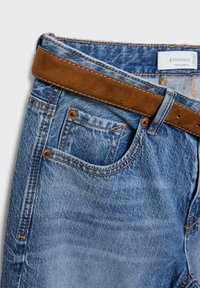 Jean en denim avec un lavage bleu clair, présentant des couturesorange, une ceinture en daim marron et cinq poches, y compris une poche pour les pièces.