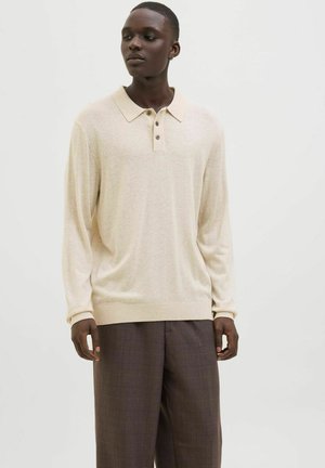 Beige langærmet polo-shirt med klassisk krave, tre-knaps lukning og ribkant; båret med brune ternede bukser.