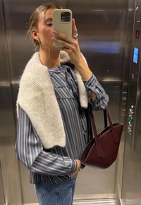 Striped blue and white blouse with a ruffled neckline, paired with a cream knitted wrap and a burgundy leather tote bag.