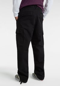 Schwarze Cargo-Hosen mit entspannter Passform, ausgestattet mit Seitentaschen, einer Gesäßtasche und einer dezenten Stofftextur. Getragen mit karierten Schuhen.