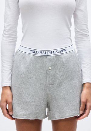 Personne portant un short gris texturé avec une ceinture élastique blanche portant l'inscription "Polo Ralph Lauren" et un haut blanc à manches longues.
