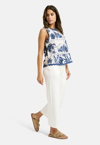 Ärmelloses Oberteil mit einem navy-blauen und weißen Blumenmuster, strukturiertem, gewelltem Saum, kombiniert mit weißen weit geschnittenen Hosen und braunen Sandalen.