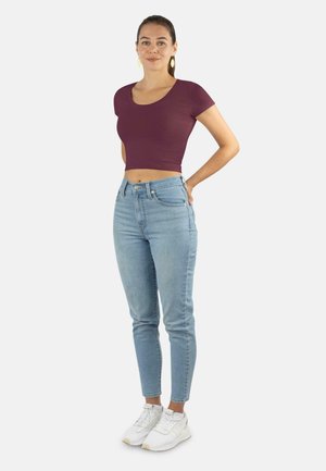 Burgunderfarbene, kurz geschnittene T-Shirt kombiniert mit hellblauen, hochgeschnittenen Jeans. Das Model trägt weiße Turnschuhe. Glatter Stoff, taillierte Passform.
