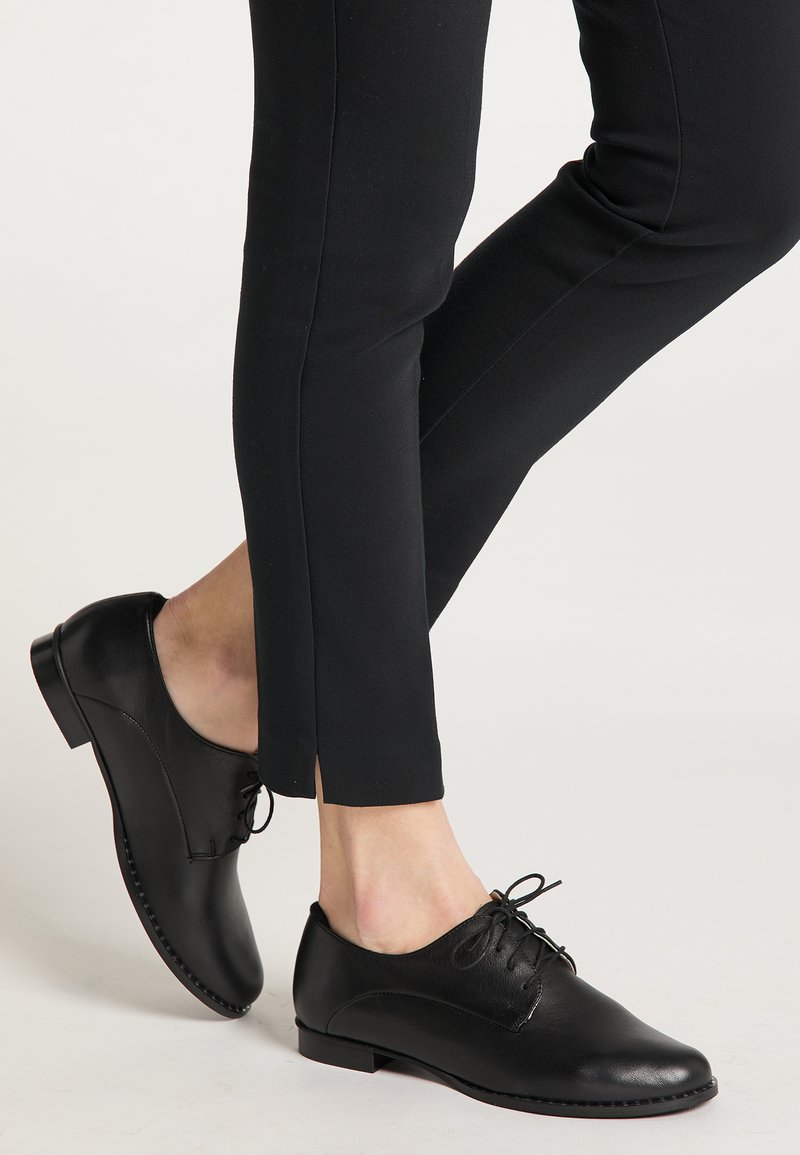 Scarpe di pelle nera con punta arrotondata e design con lacci. Texture liscia, tacco basso e dettaglio di cucitura discreto. Indossate con pantaloni neri.