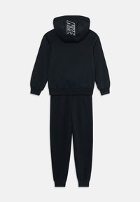 Survêtement noir Nike avec sweat à capuche arborant le logo Nike blanc sur la capuche, associé à un pantalon de jogging assorti avec des poignets côtelés.